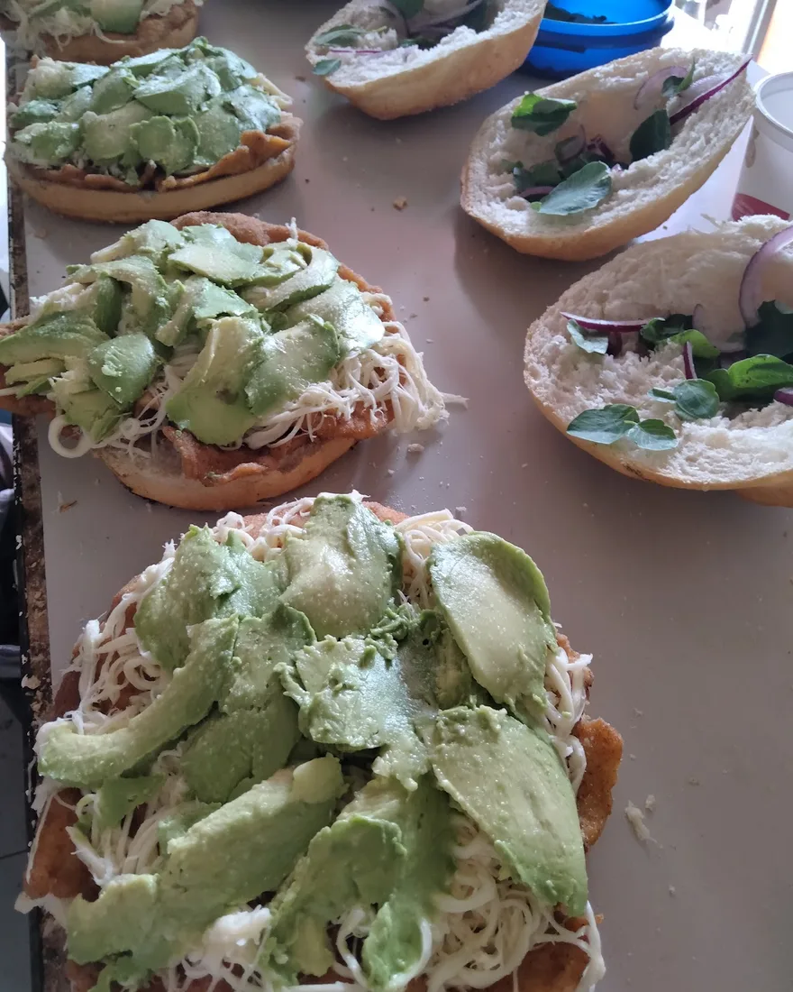 Cemitas abiertas con milanesa, quesillo y rebanadas de aguacate, listas para cerrarse